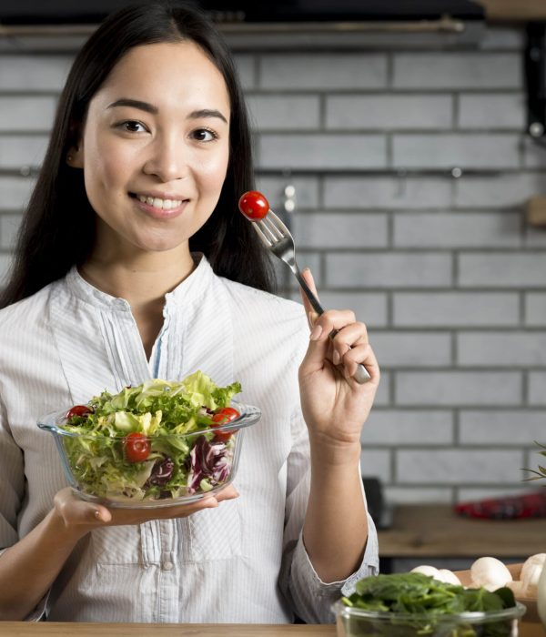 young-woman-holding-fork-with-tomato-healthy-salad-standing-kitchen-min